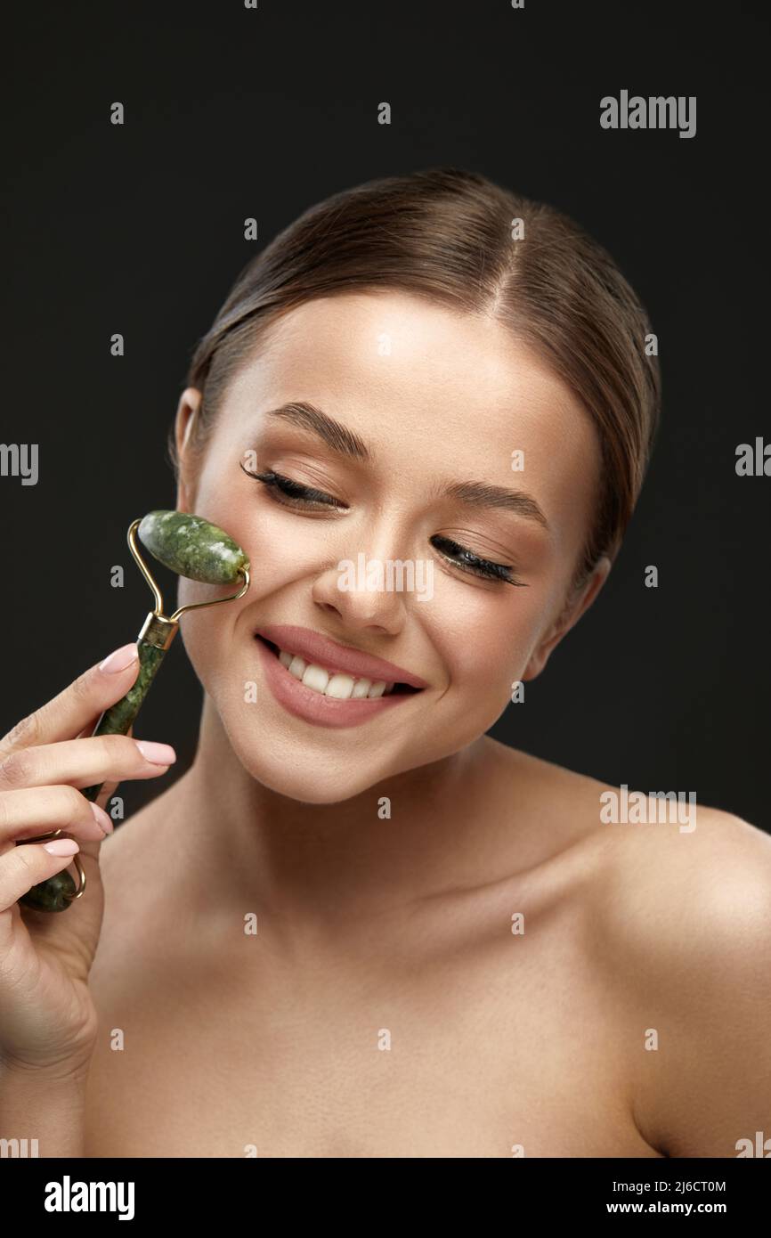 Beauty Skin Care. Face Massage. Woman Using Jade Facial Roller For Face Massage At Home. Girl Using Natural Massager For Spa Treatment. Stock Photo