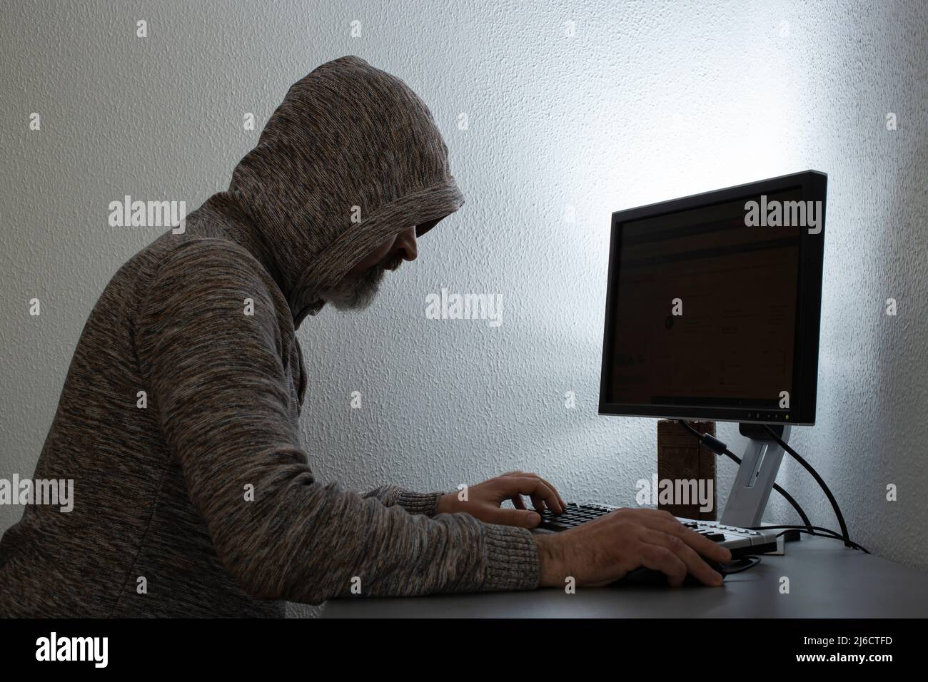 bearded man with a hoodie, hacking on a black screen computer Stock Photo