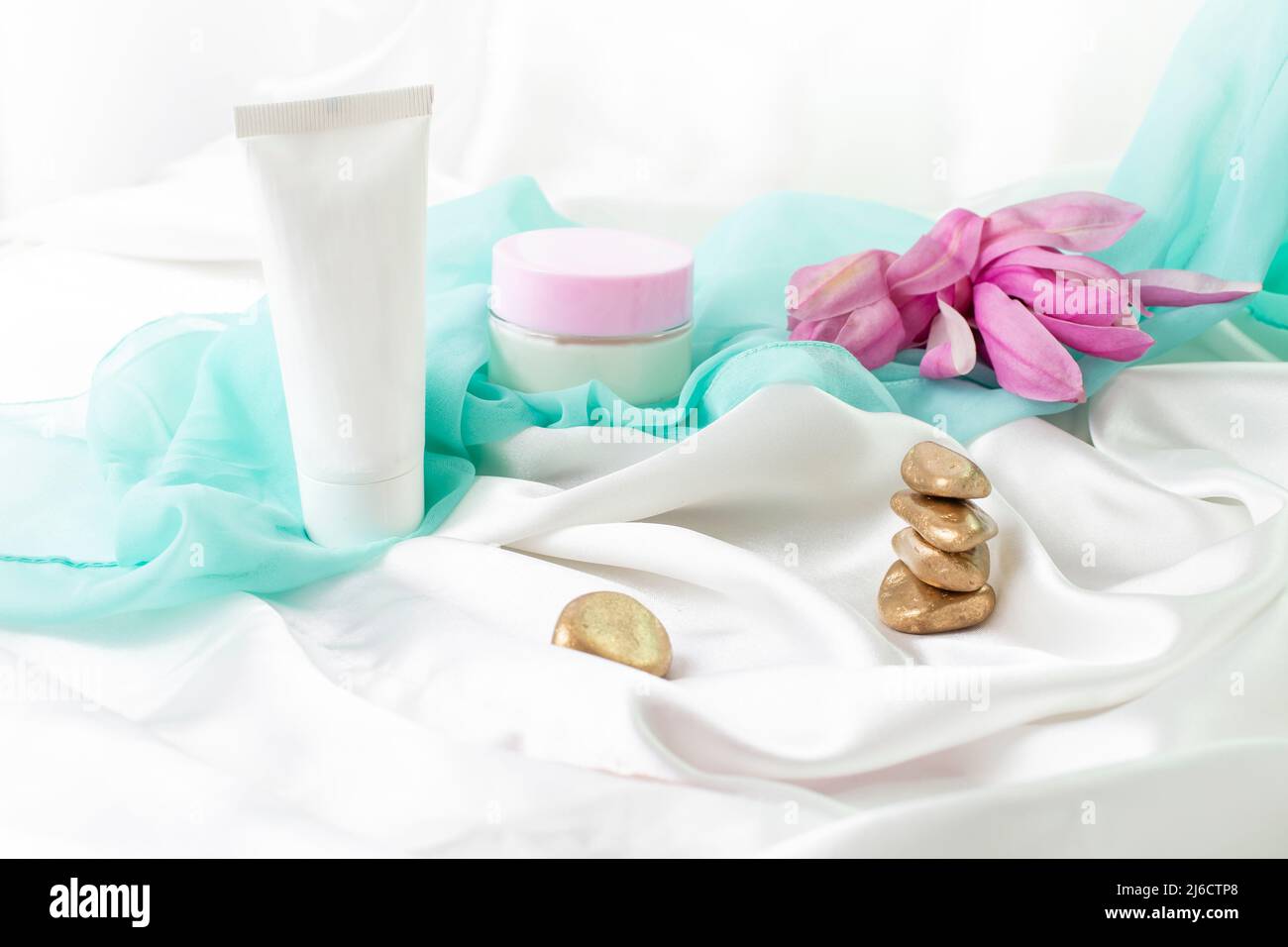 tube and jar without label, product mockup for skin care products, with white satin golden zen stones and magnolia flowers Stock Photo