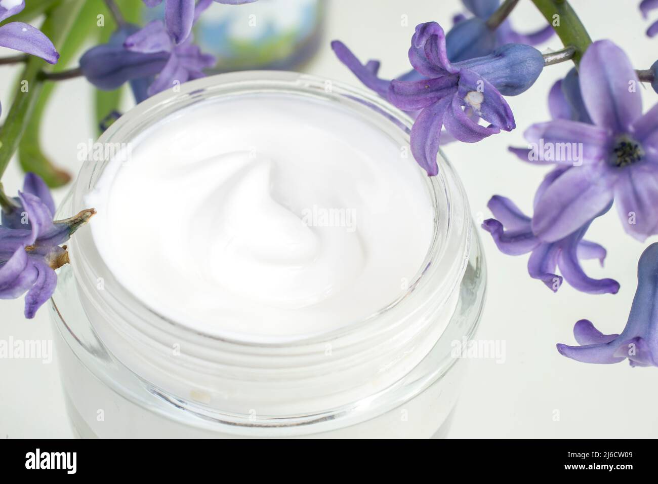 Cosmetic cream texture in a glass jar, next to hyacinthus purple flowers Stock Photo
