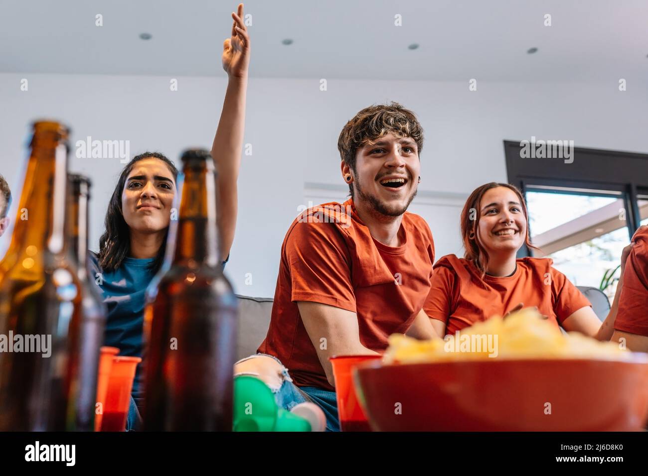 friends hugging after the victory of their sports team broadcast on television. group of young people partying at home. Stock Photo