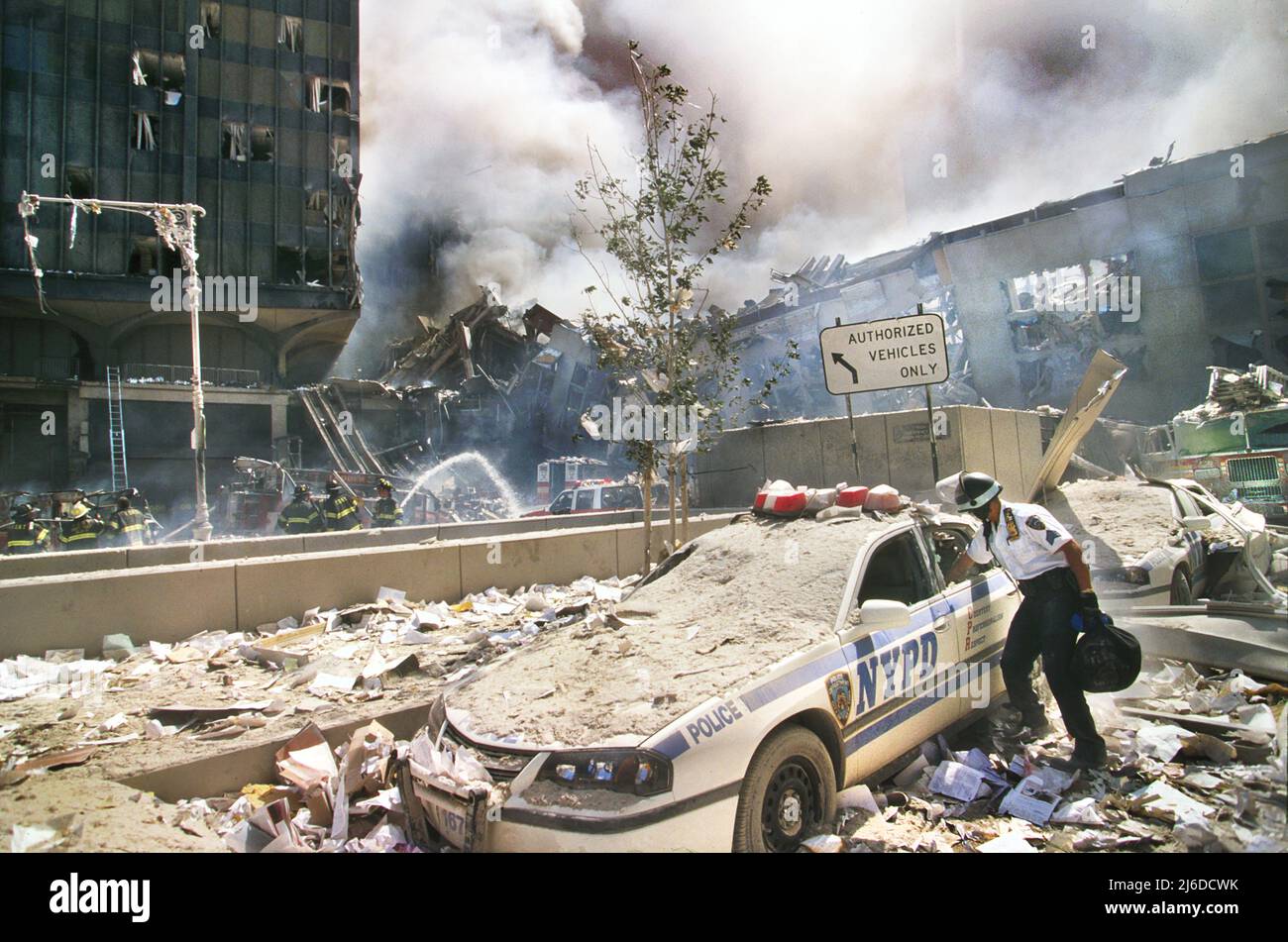 Rescue worker reaching into a New York Police car covered with debris with smoldering ruins in background, Terrorist Attack on World Trade Center, New York City, New York, USA, Unidentified Artist, September 11, 2001 Stock Photo