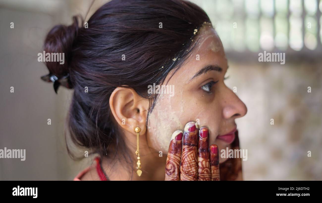 Beautiful woman is washing facial mask in bathroom after applying face mask. Girl spraying water on her face standing in front of mirror at home. mud Stock Photo