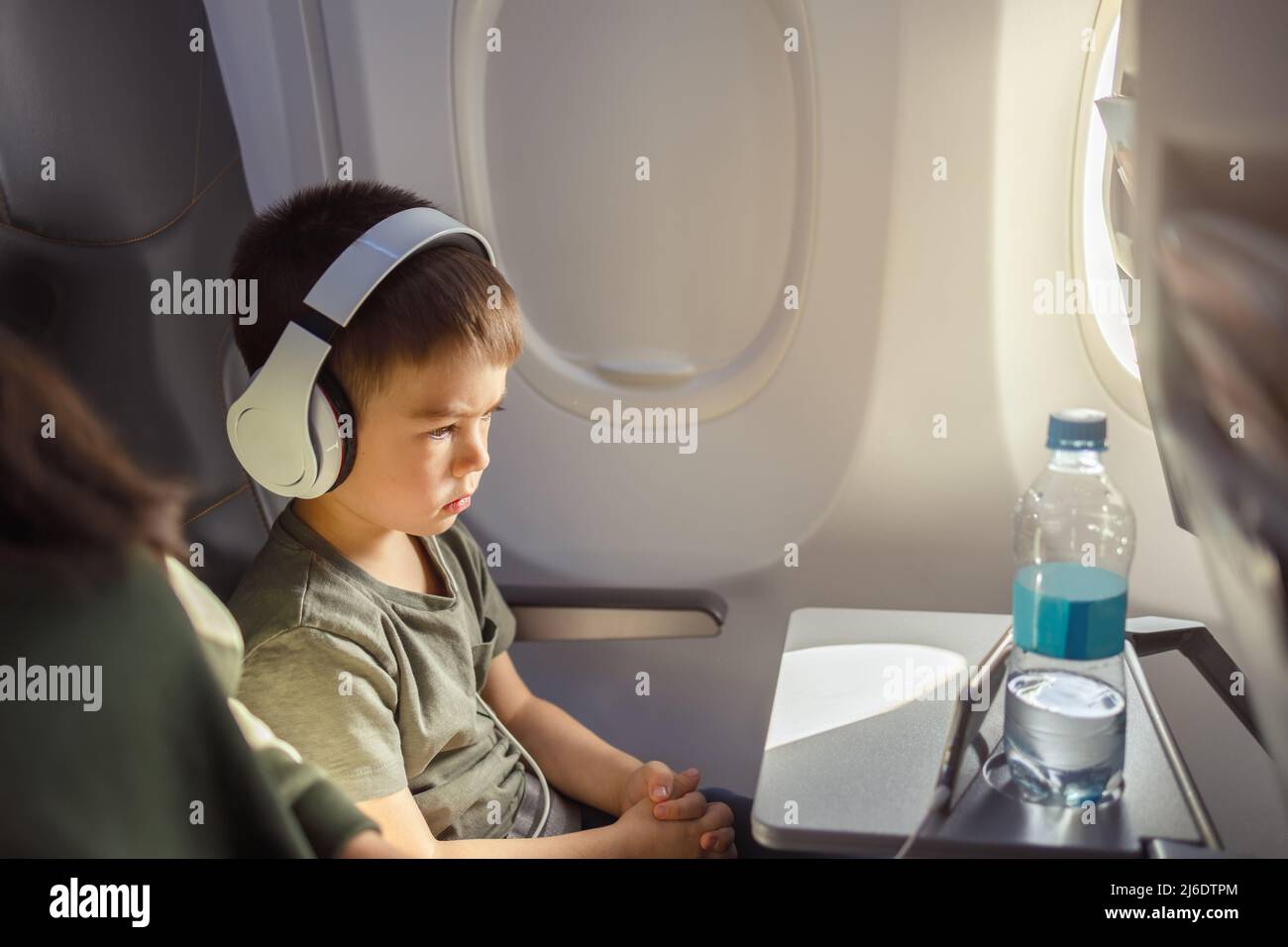 little boy in headphones with smartphone near window in aircraft Stock Photo