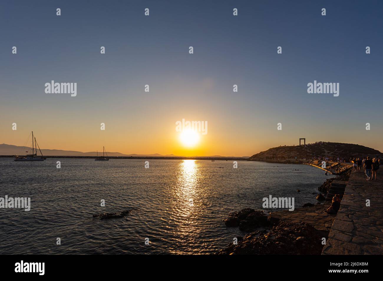 Sunset in Naxos Bay. The red and yellow glowing sun sinks on the horizon. Boats anchor and lie off the coast. Romantic scene in the Cyladen archipelag Stock Photo