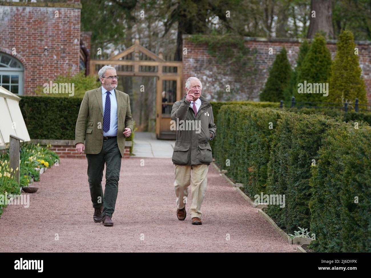 The Prince of Wales, Patron of The Queen's Green Canopy (QGC) alongside Head Forester Geraint Richards (left), as they walk through the walled gardens on their way to view the 'Old Sycamore' in the Dumfries House garden, as he unveils a nationwide network of seventy ancient woodlands and seventy ancient trees, including the sycamore, to be dedicated to his mother, Queen Elizabeth II, in celebration of the Platinum Jubilee. Picture date: Monday April 25, 2022. Stock Photo