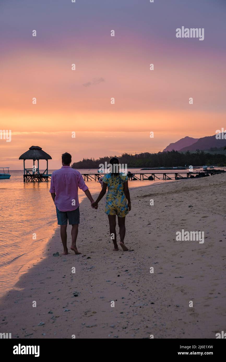 couple watching the sunset on a tropical beach with a wooden pier in ...