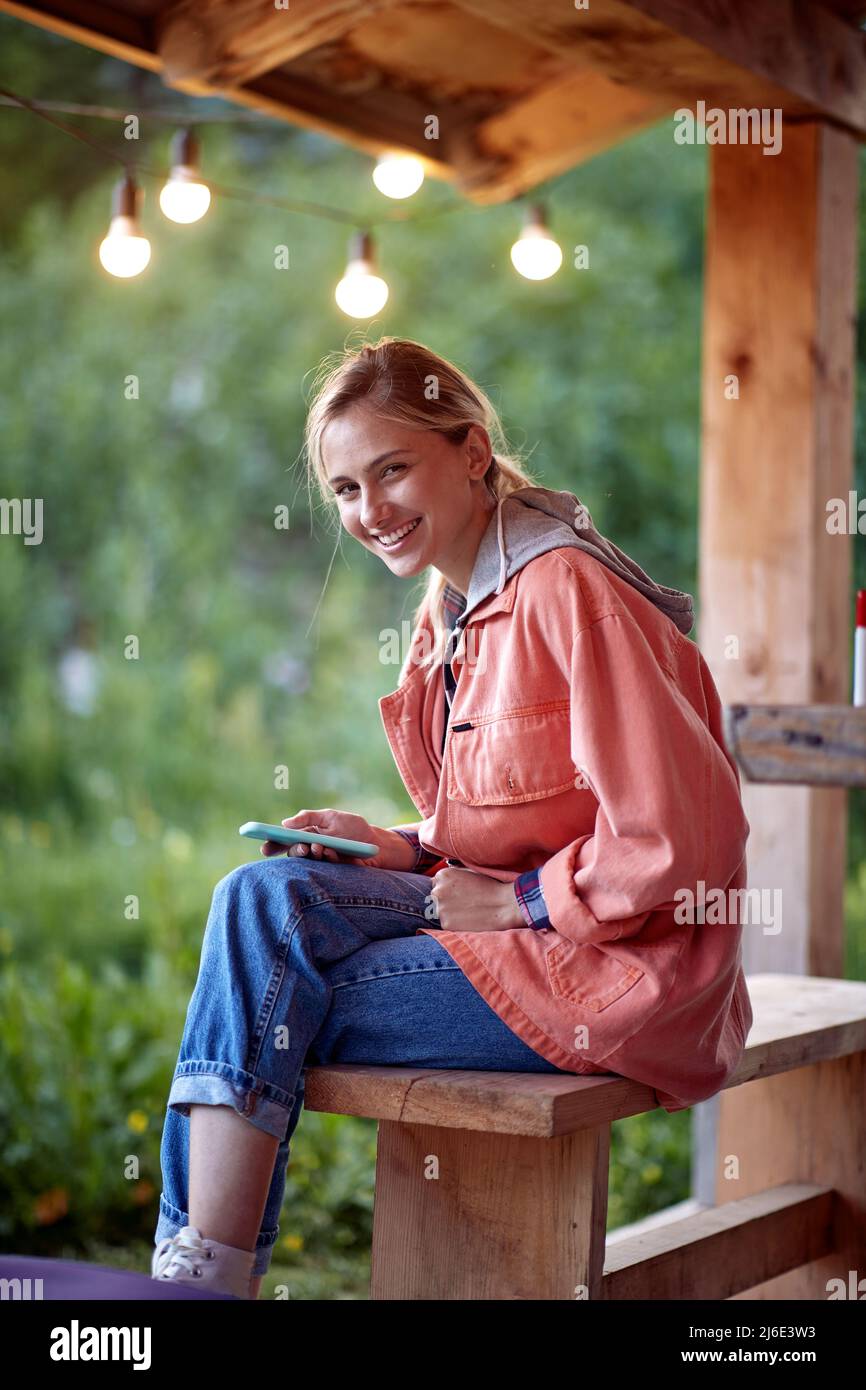 A young girl is sitting at the cottage porch in the forest and posing for a photo on a beautiful day. Vacation, nature, cottage Stock Photo