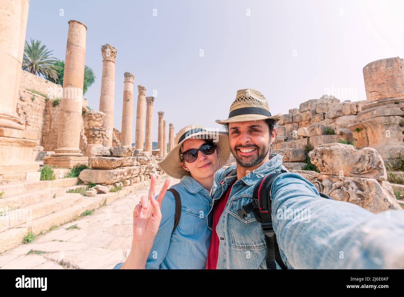 a young couple with hat taking a selfie while enjoying the beautiful landscape of the ancient ruins of Jerash in a sunny day Stock Photo