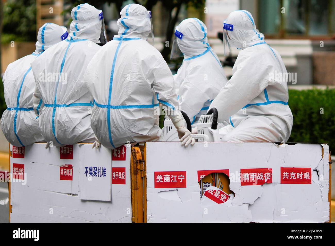 Workers in protective suits ride an electric tricycle on a street