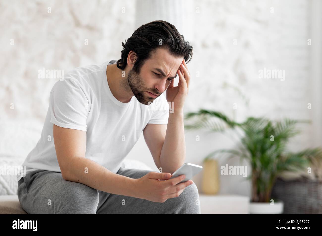 Upset young man using smartphone in bed Stock Photo