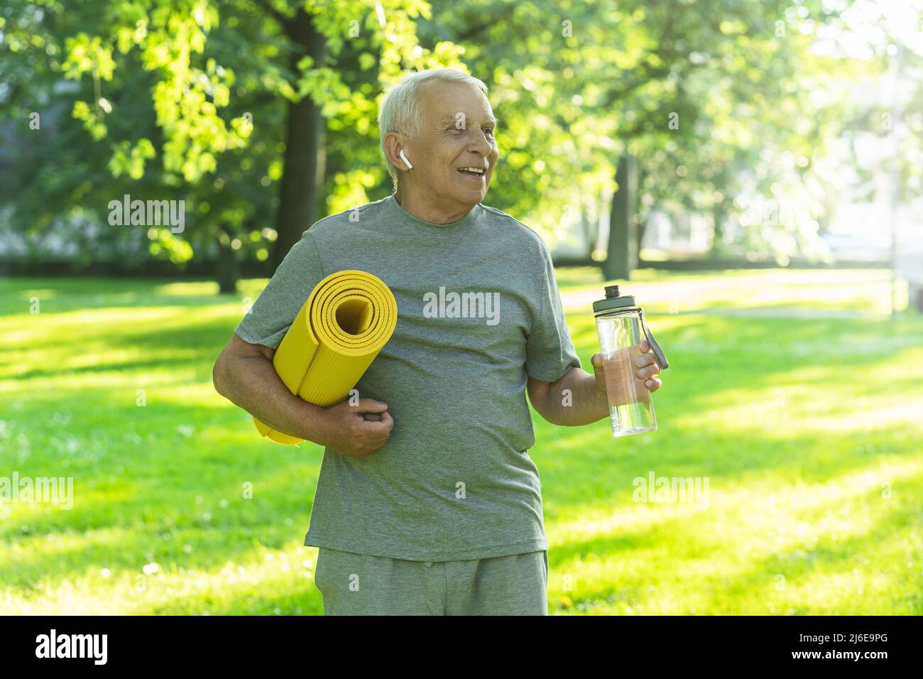 Active elderly man with a exercise mat and bottle of water in green ...