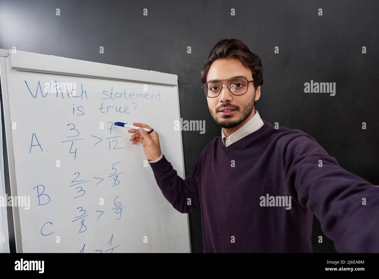 Portrait of young Mixed race teacher with stubble pointing at whiteboard while explaining new material and shooting video Stock Photo