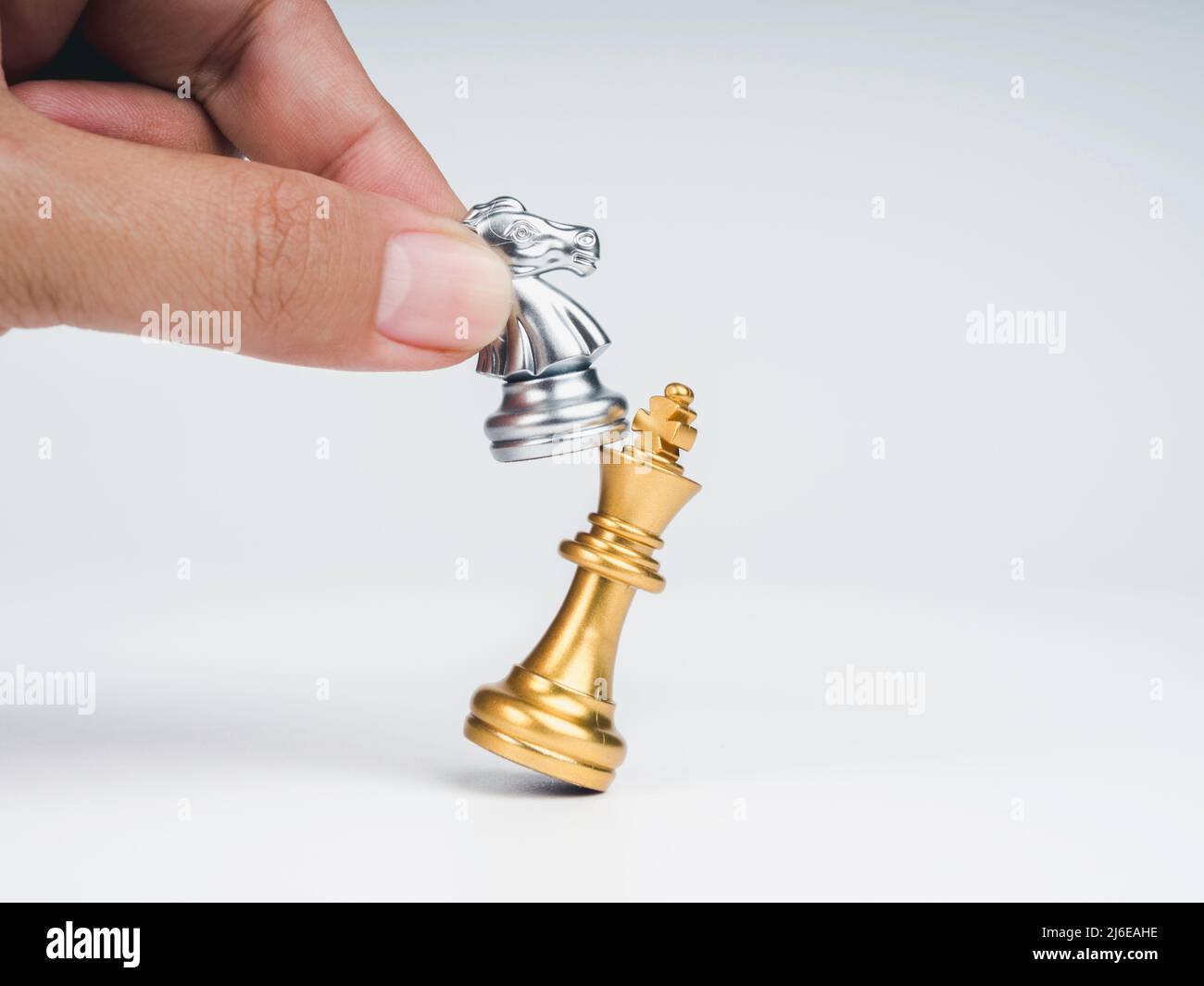 Close-up horse, silver knight chess piece attack the gold king isolated on white background. Hand moving chess figure on chess game competition. Strat Stock Photo