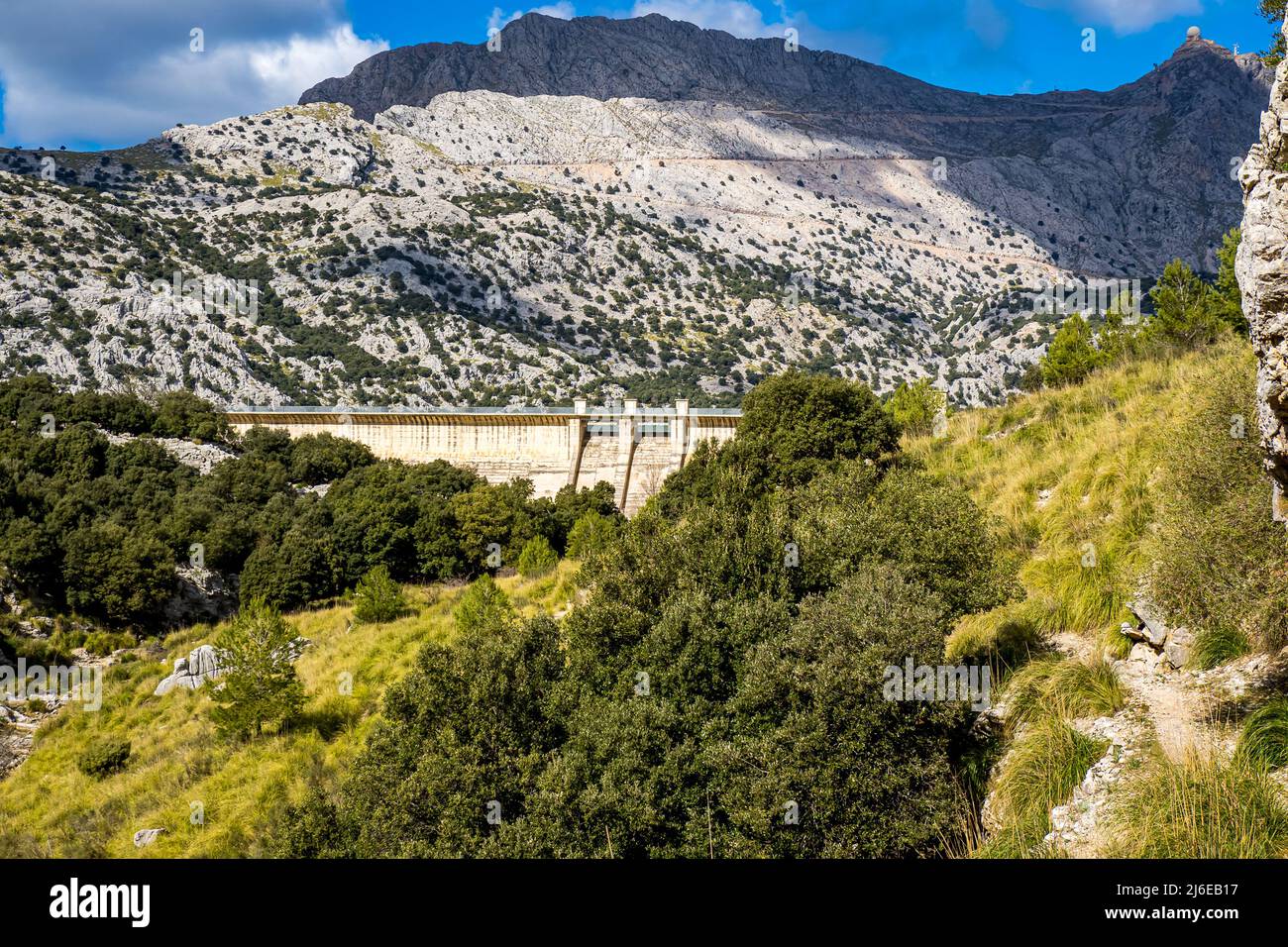 Panorama of grassy valley Torrent d'Aumadrá with dried up watercourse protected with the dam of Embassament de Cúber in the background below mountains Stock Photo