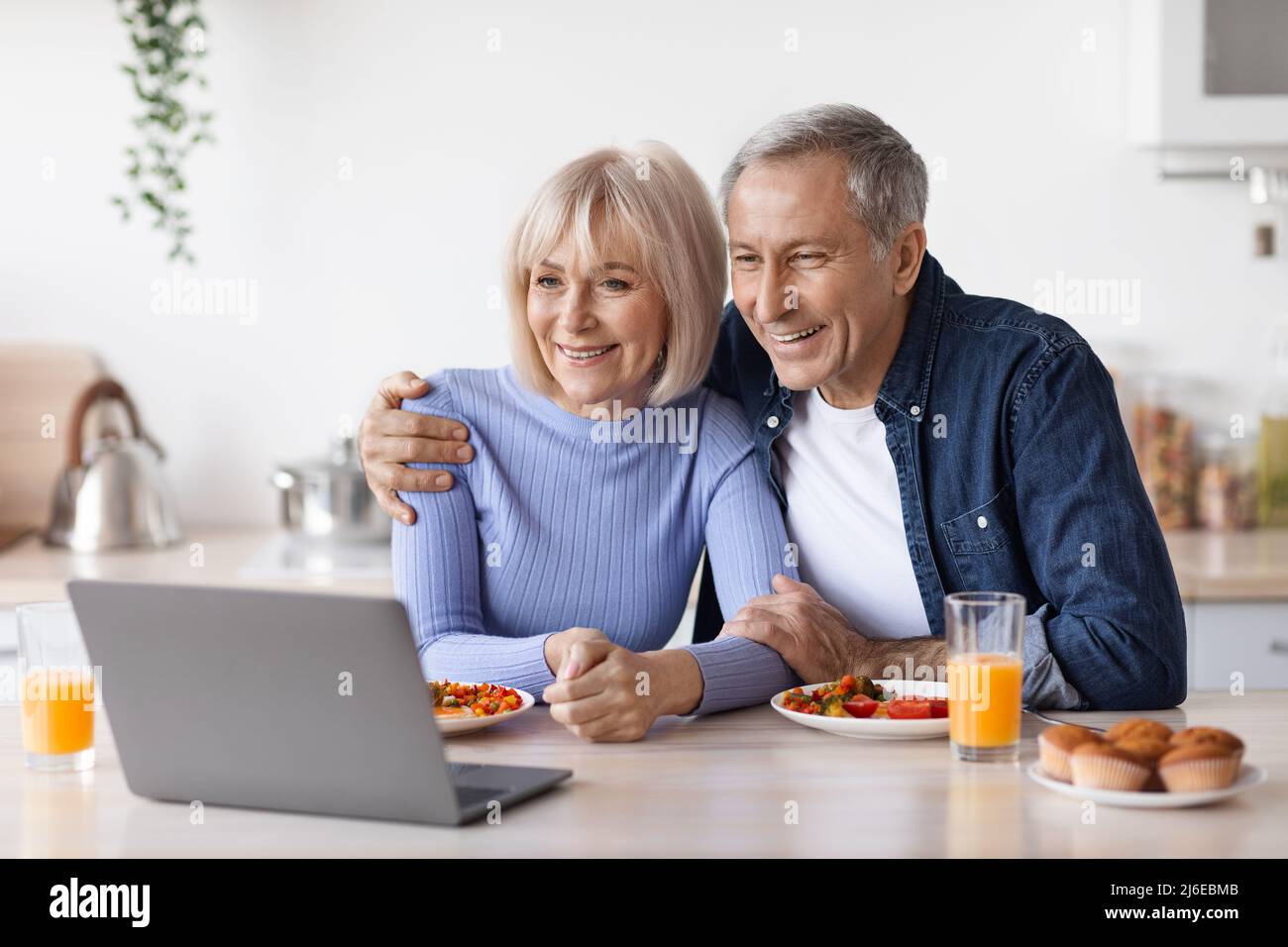 Cheerful senior couple using computer while having breakfast Stock Photo