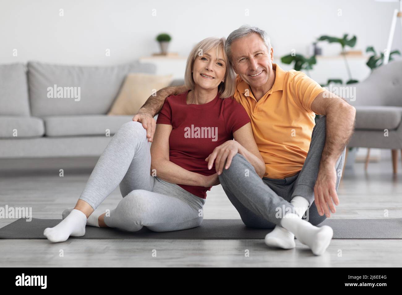 Happy elderly couple sitting on fitness mat at home Stock Photo