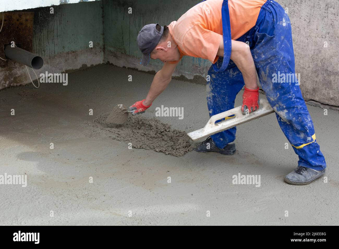 Stormwater construction. An anonymous male construction worker in blue work overalls and an orange construction T-shirt builds a rainwater storm drain Stock Photo