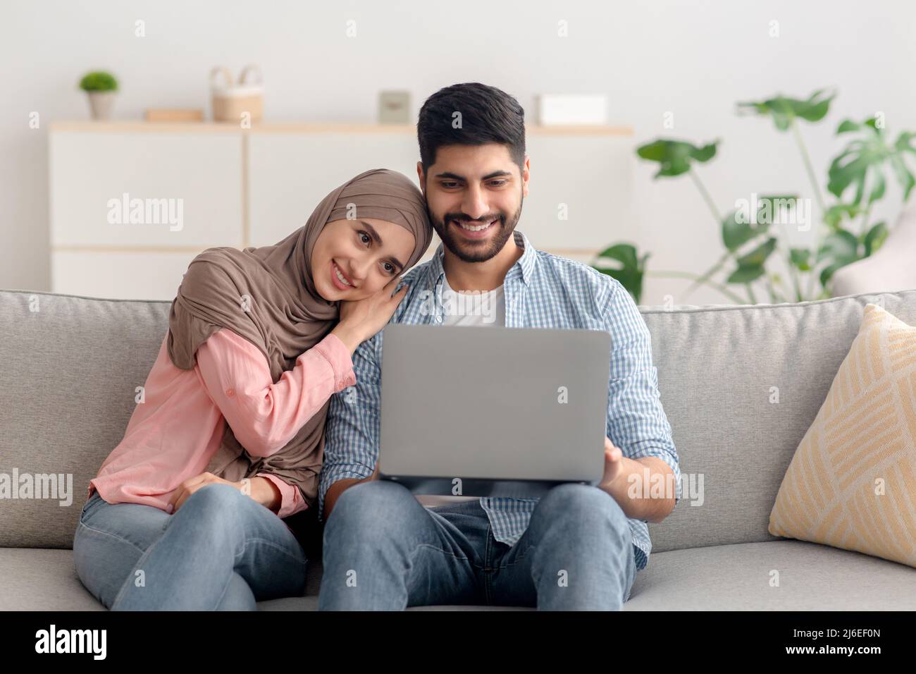 Happy Middle Eastern Spouses Using Laptop Sitting At Home Stock Photo