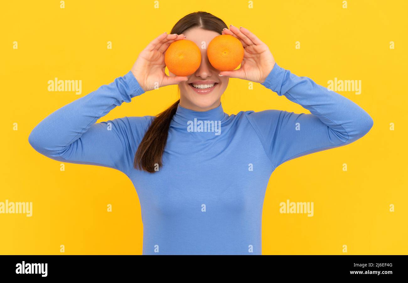funny young woman holding orange citrus fruit on yellow background, vitamin Stock Photo