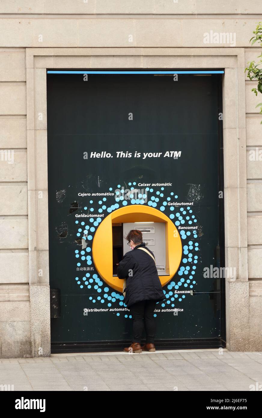 Woman using ATM with multi lingual signage, Tarragona Stock Photo