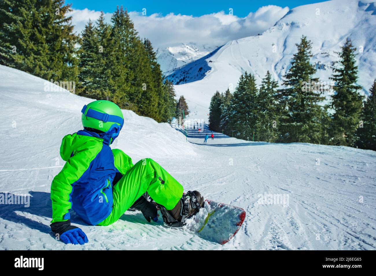 Boy sit on the ski track with snowboard attached look downhill Stock Photo