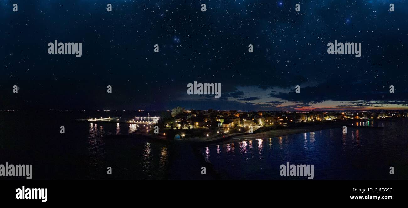 Panorama of night sea luminous city of Pomorie with modern comfortable resort hotels and bright evening electric lights, bathed by dark calm Black Sea Stock Photo
