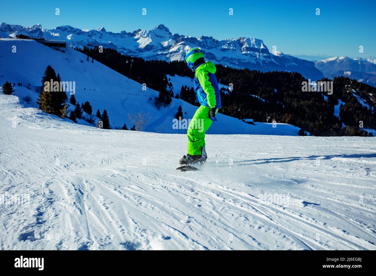 Boy about to go downhill on snowboard with tops of mountain Stock Photo