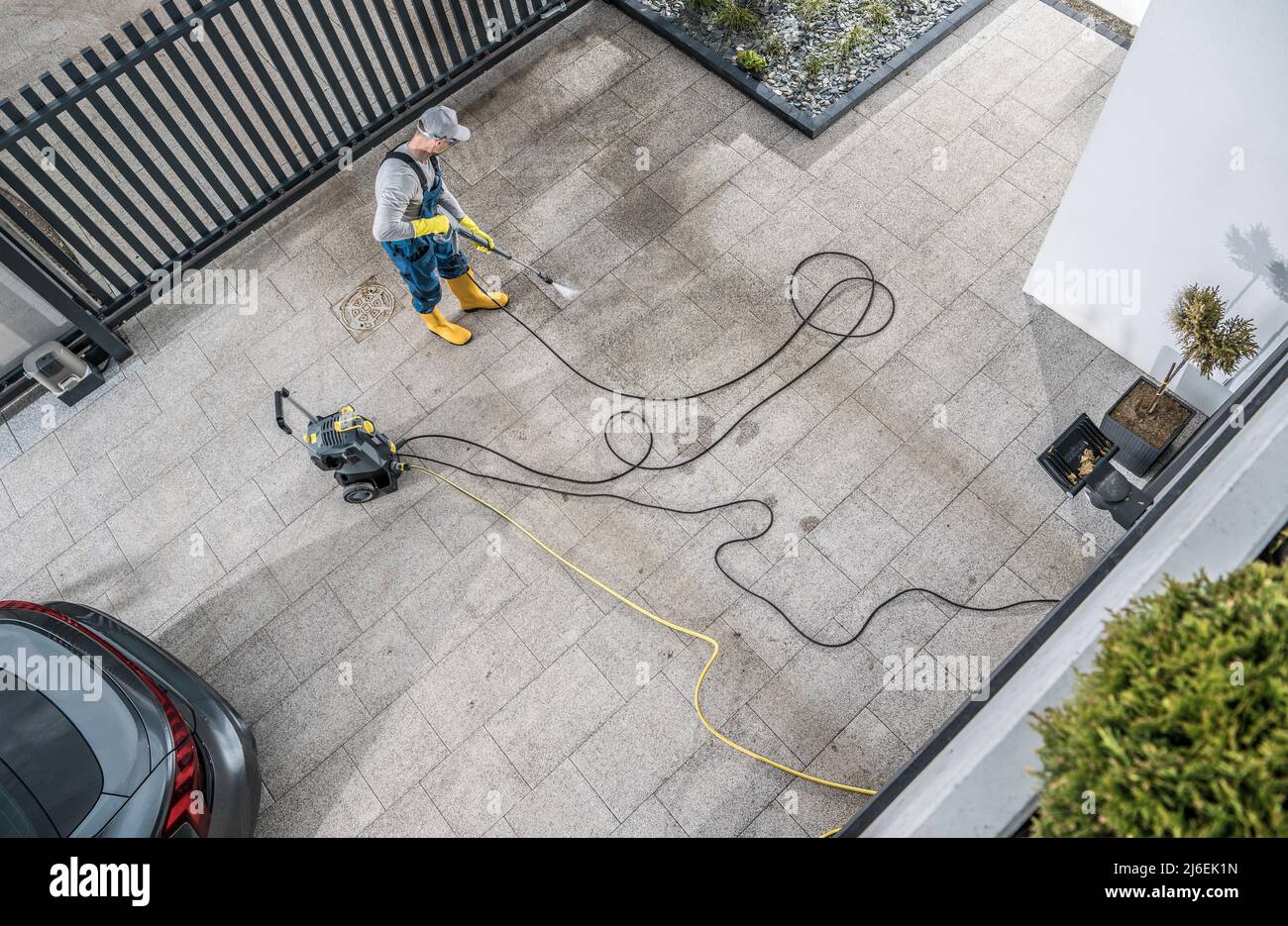 Caucasian Home Owner Pressure Washing His Dirty Driveway Aerial Photo. Keeping Concrete Driveway Bricks Clean. Stock Photo