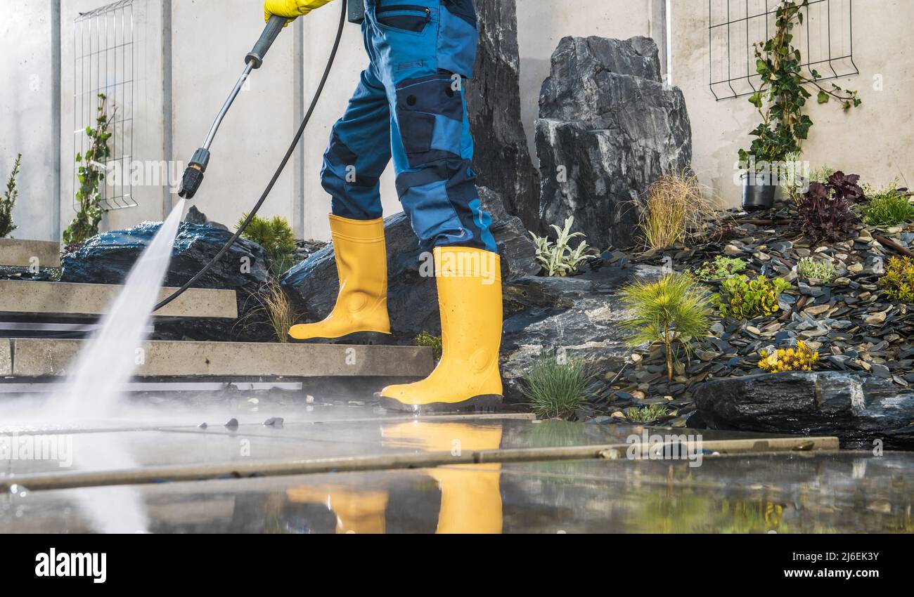 Men Wearing Yellow Rubber Boots Pressure Washing Architectural Concrete Elements in His Garden. Lower Body Close Up. Modern Concrete Backyard Stairs C Stock Photo