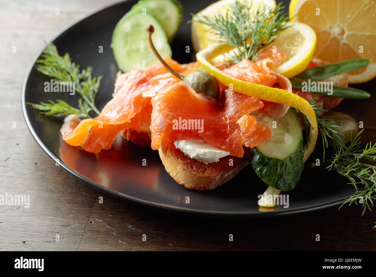 Sandwich with salmon, cream cheese, dill, cucumber, capers, green onion, and lemon. Stock Photo