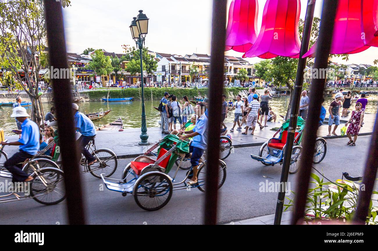 View of tourists and river from inside a restaurant through the bars on the window. Bicyle carriages pass by to take tourists for rides. Stock Photo