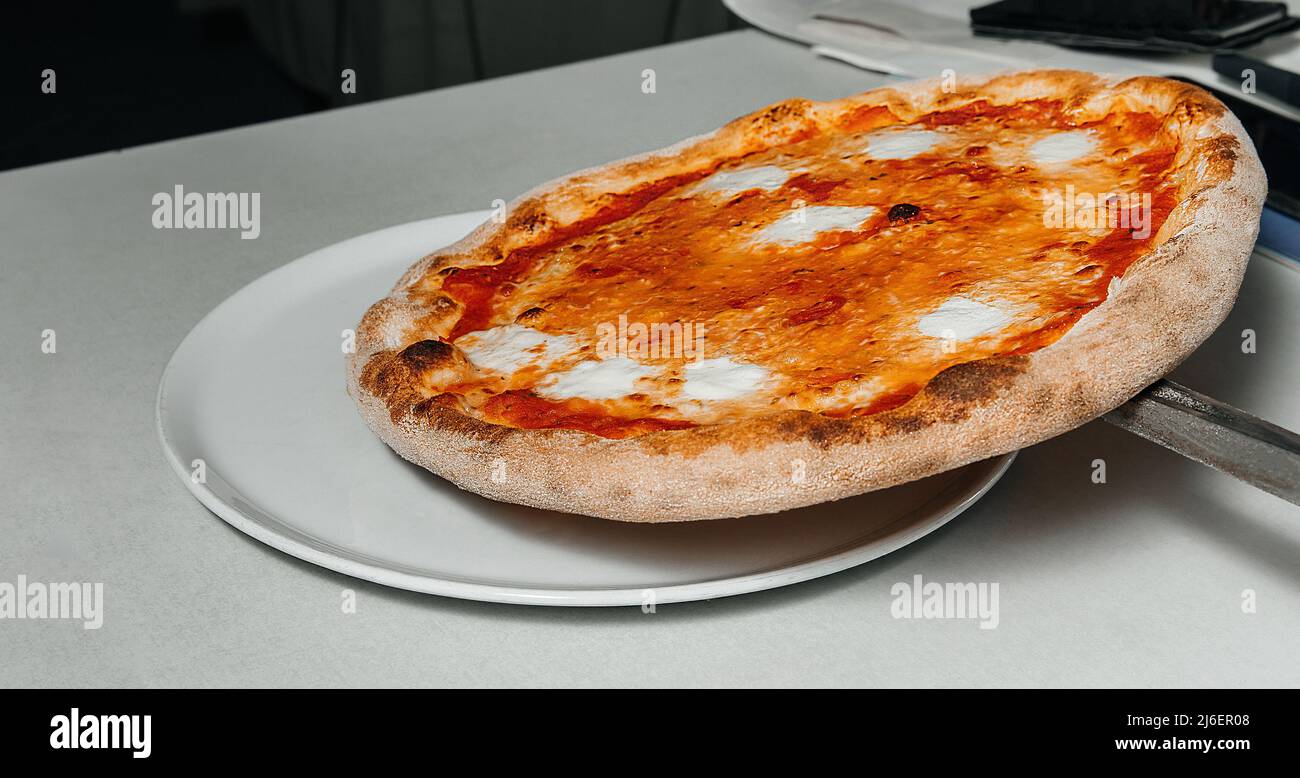 Process of placing pizza with mozzarella, tomato, cheese from oven at pizzeria, restaurant kitchen concept Stock Photo