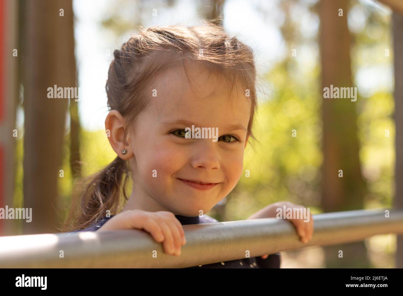 Little beautiful girl with braided pigtails has fun on the uneven bars