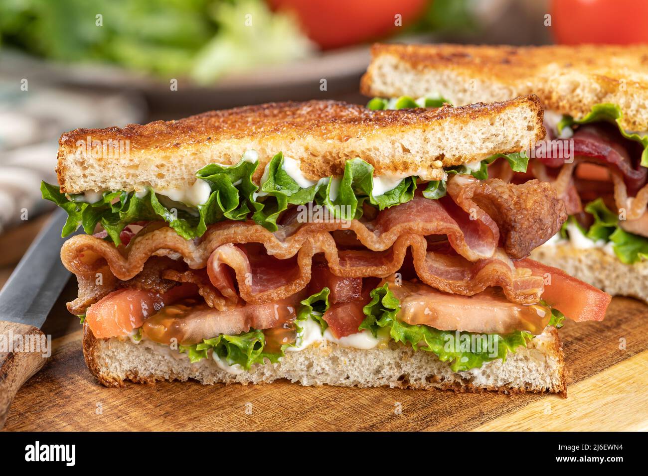 Closeup of blt sandwich made with bacon, lettuce and tomato on toasted whole grain bread cut in half on a wooden cutting board Stock Photo