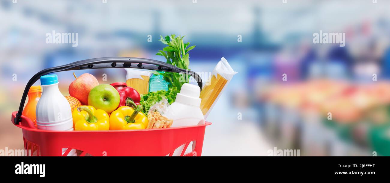 Shopping basket filled with goods, supermarket aisle in the background, grocery shopping concept Stock Photo