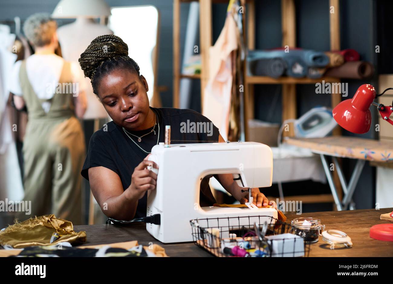 Young serious black woman in casualwear sewing new fashionable attire for clients of her boutique or creating seasonal collection of clothes Stock Photo