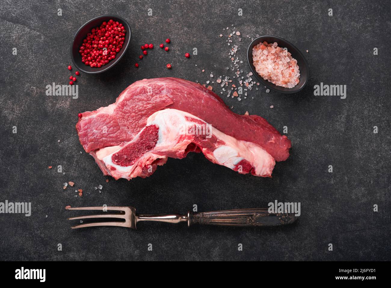 Raw beef meat. Rough piece of meat on bone for roast or soup with salt, pepper, thyme and rosemary on a black concrete background. Entrecote. Raw cowb Stock Photo