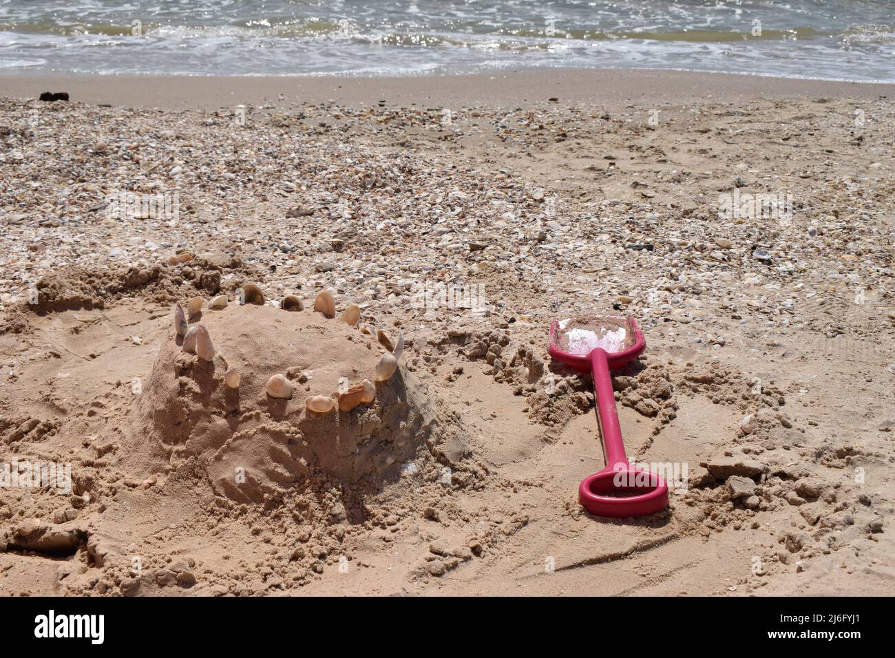 Sand castle with shells built on summer tropical beach. Close up of spade and shells on a beach. Stock Photo