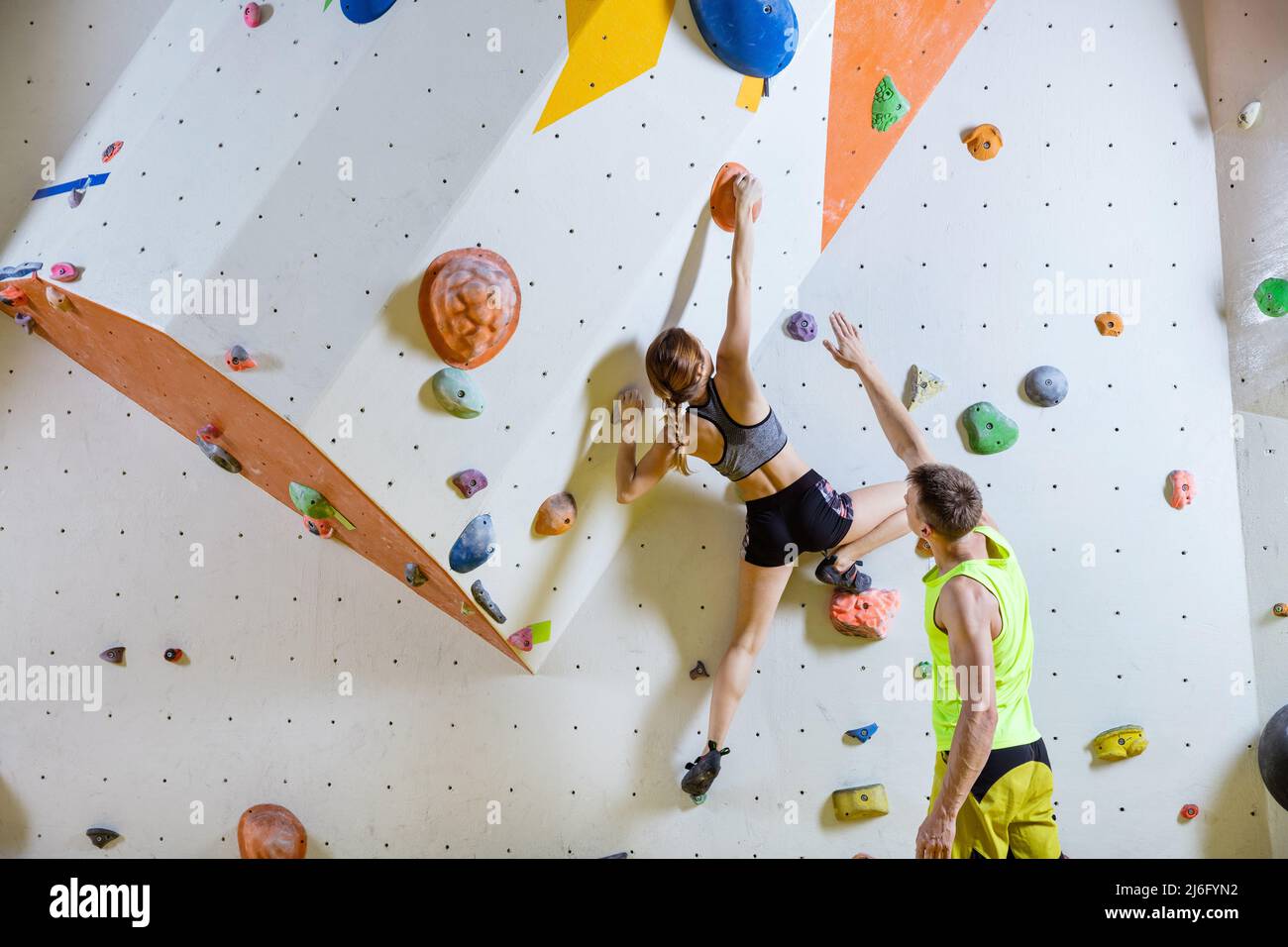 Rock climbers in climbing gym. Young woman climbing bouldering problem (route), man giving her