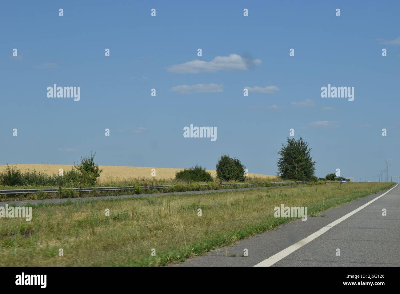 Cars drive on the highway, the road outside the city among the fields in summer. Highway road in the countryside, roadside and gray asphalt, green tre Stock Photo