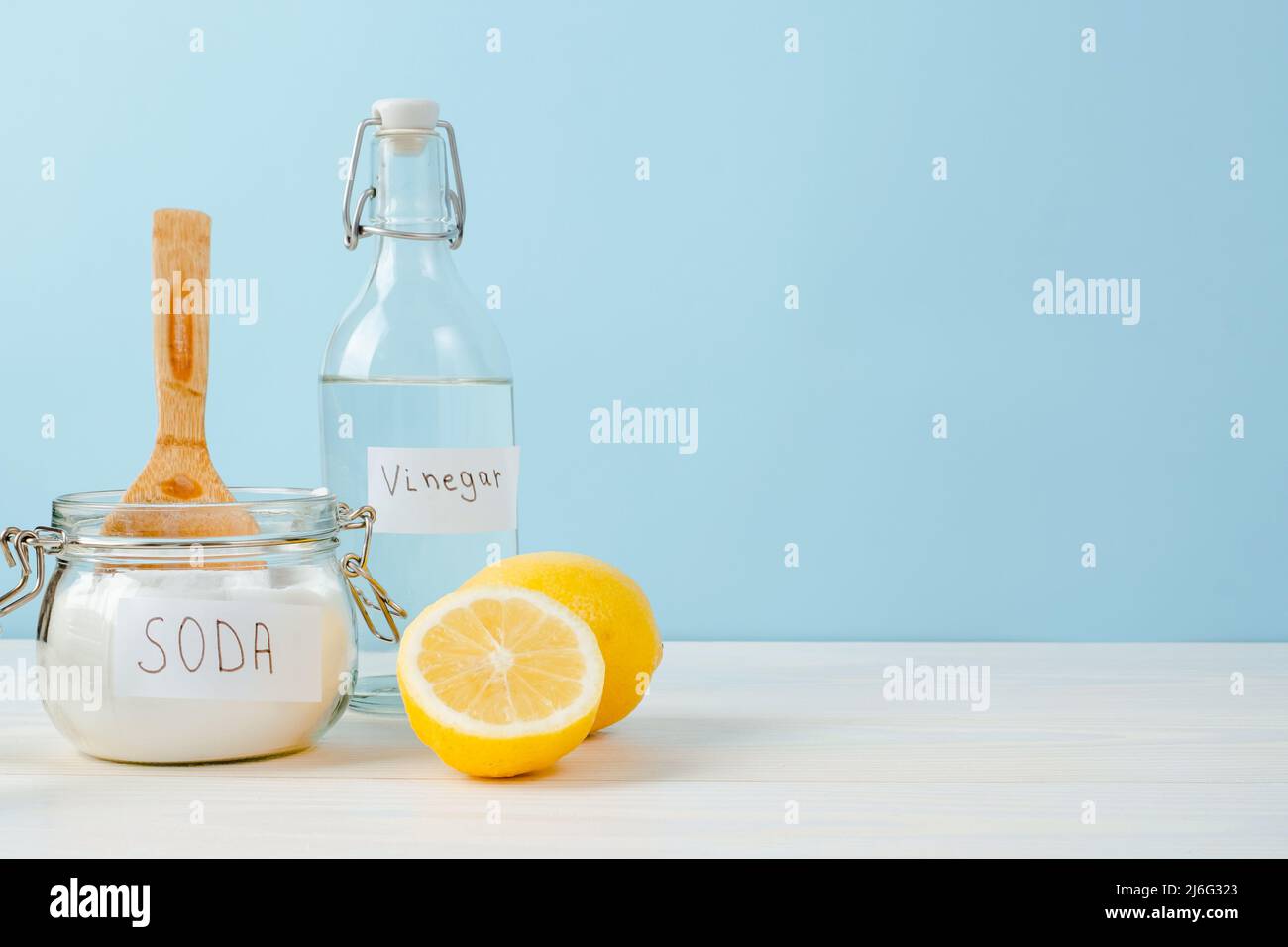 Open jar of baking soda with a wooden spoon on top, vinegar, cut lemon, on a blue background. The concept of organic removing stains on clothes. Stock Photo