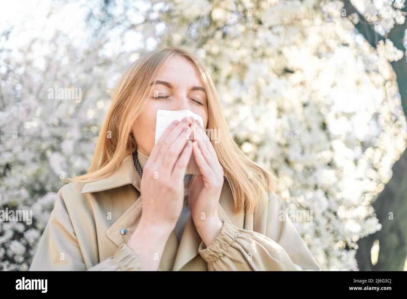 Young woman with handkerchief sneezing because of spring pollen allergy, seasonal allergy outdoors Stock Photo