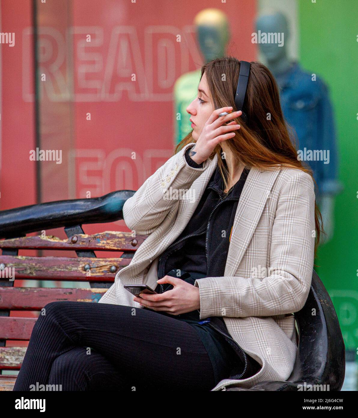 A beautiful young woman seated outside relaxing in the warm Spring sunshine while smoking a cigarette in Dundee city centre, Scotland Stock Photo