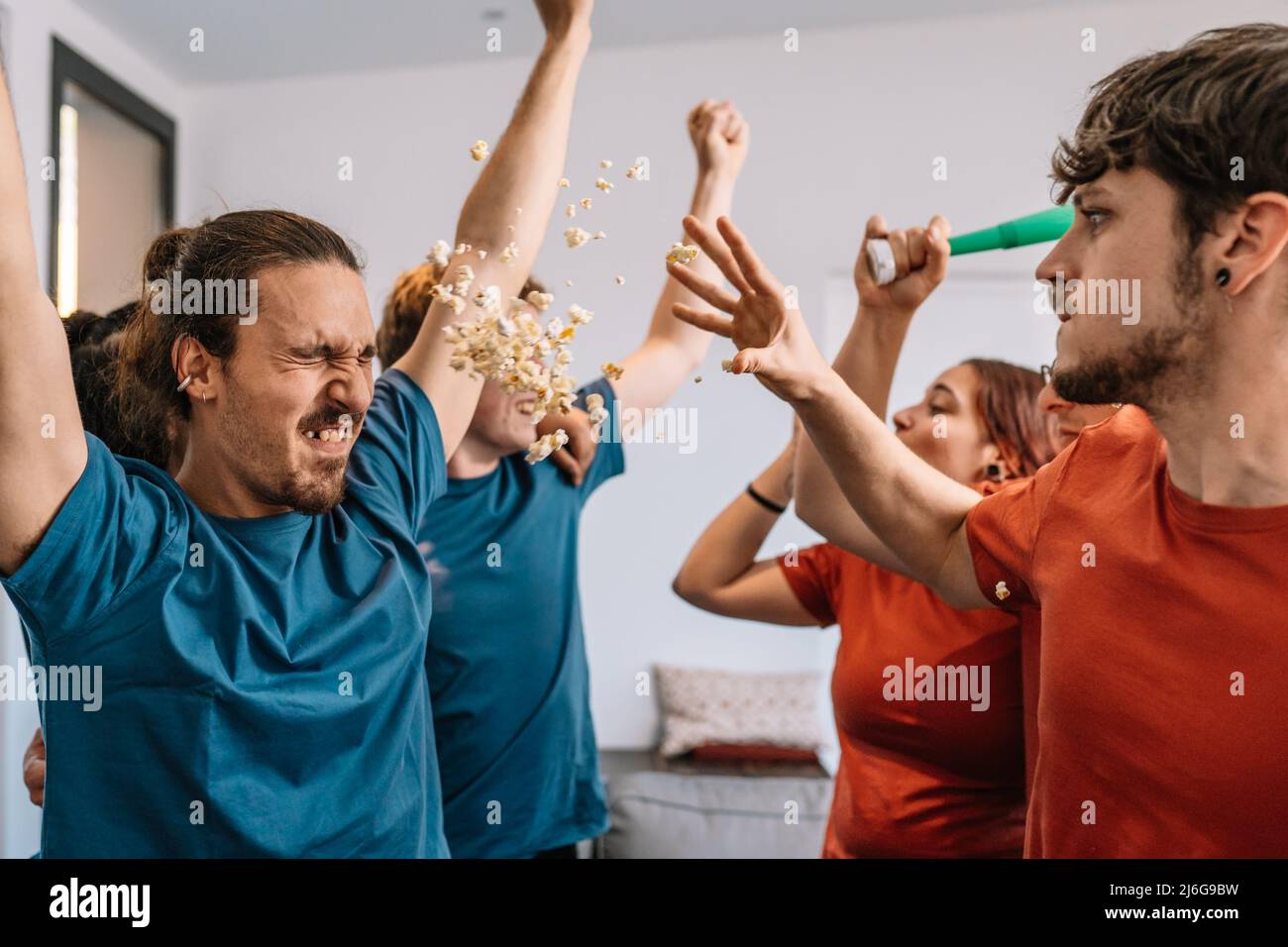 friends celebrating a sports championship on TV. losing team throws popcorn at the winning team. e-sports. soccer. Stock Photo