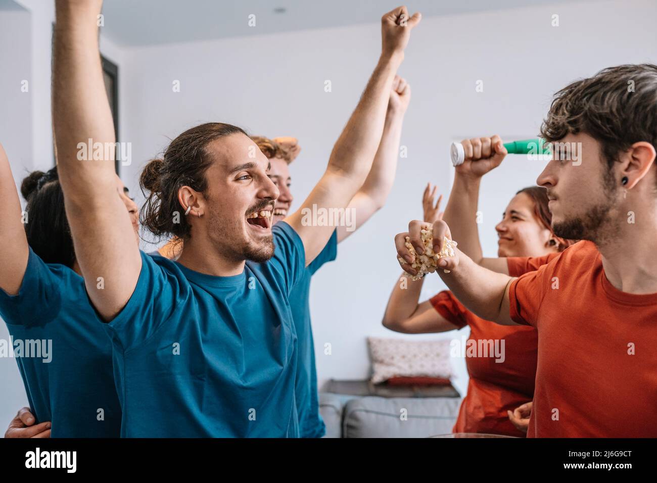 group of friends watching a sports championship on TV losing team throws popcorn at the winning team. leisure concept. Stock Photo