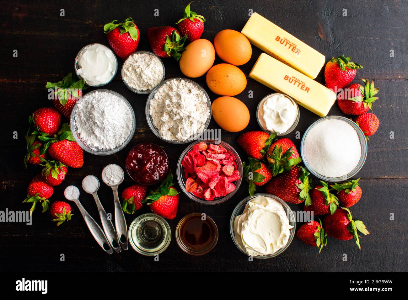 Fresh Strawberry Cake Ingredients on a Dark Wood Table: Fresh strawberries, flour, butter, and other cake ingredients on a dark rustic background Stock Photo
