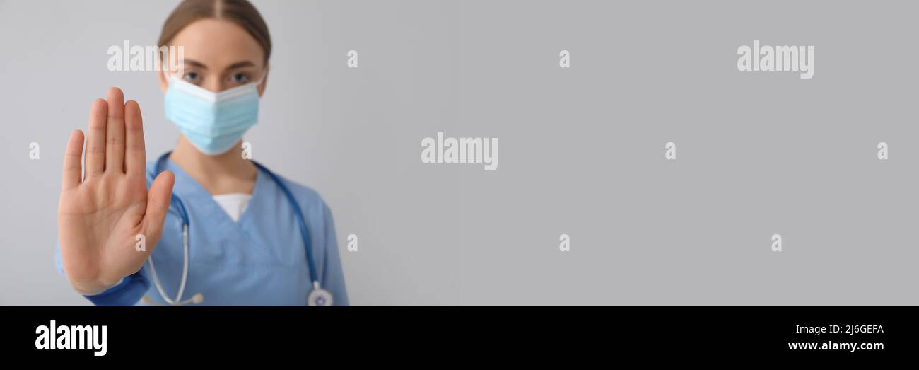 Female nurse in medical mask showing STOP gesture on grey background ...