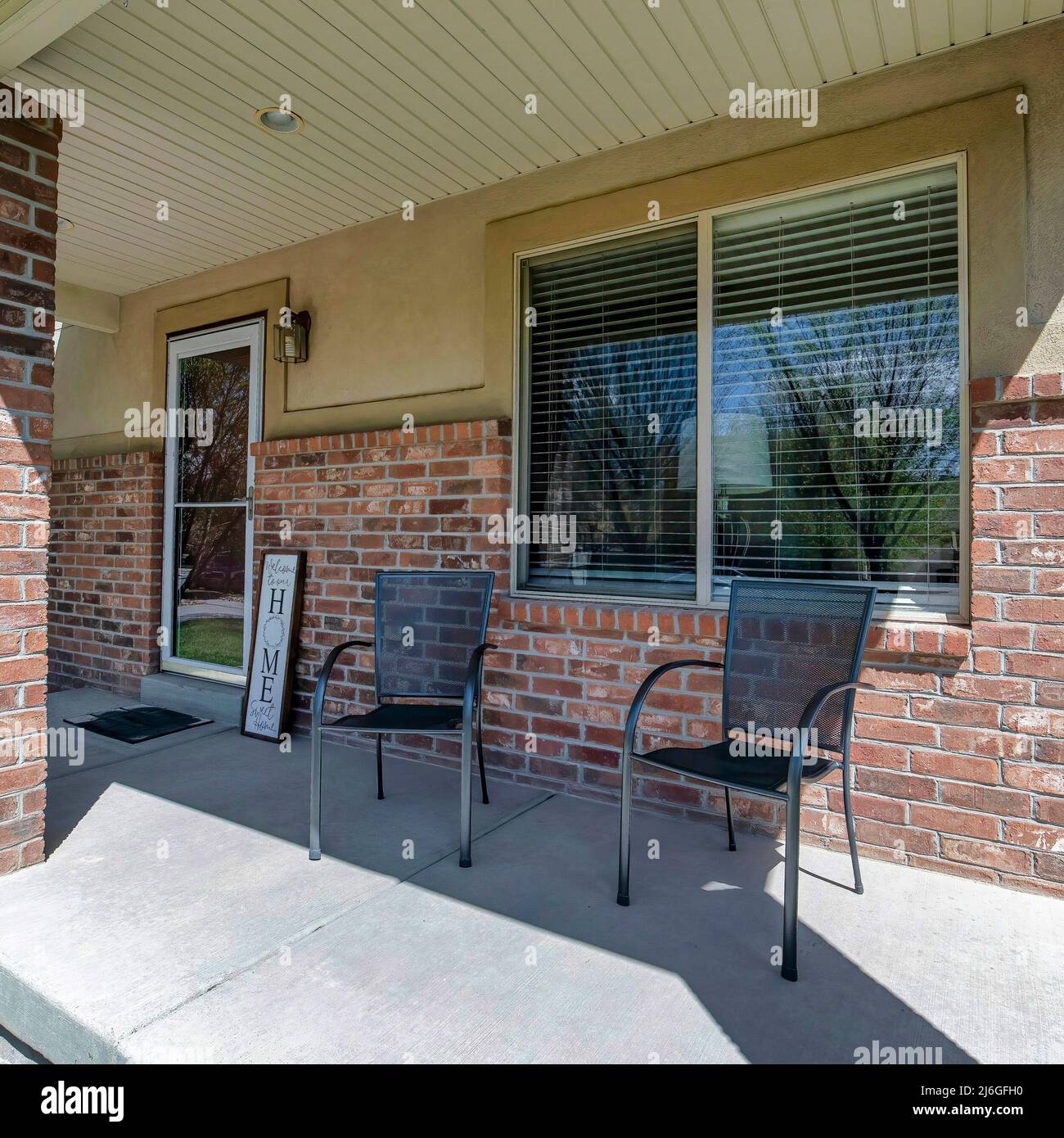 Square Front porch of a house with two chairs and signboard near the ...