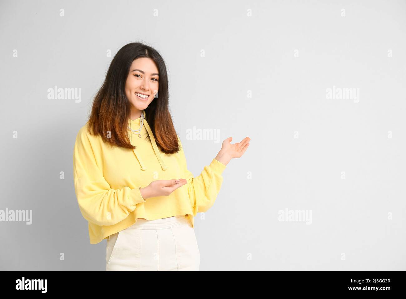 Inviting young Asian woman showing something on light background Stock ...